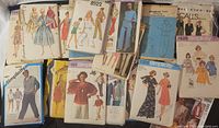 A collection of vintage sewing pattern envelopes laid out showing various illustrated designs of women's dresses, jumpsuits, and men's casual wear by Simplicity, McCall's and Vogue.