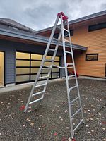 Front angle view of an open 10-step aluminum step ladder with red top cap and braces, standing on driveway.