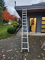 Ladder extended against building showing about 26 steps and blue rope securing it.