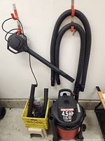 Craftsman shop vac with hose and attachments hanging on garage wall with yellow crate containing accessories.