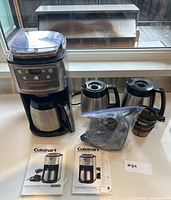 Full view of Cuisinart burr grind and brew coffeemaker with thermal carafe, an additional carafe, accessories in a plastic bag, and instruction booklets on countertop