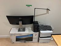 Dell UltraSharp 34" monitor with original box, Dell speaker system, StarTech docking station boxes and wrapped keyboard on table