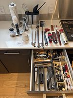 Kitchen countertop showing cleaning brush, utensil holder with whisk and spatulas, a soap dispenser, and assorted stainless steel cooking utensils.