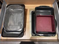 View of stack of metal roasting pans with wire rack and non-stick bake trays including red silicone mold
