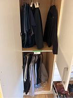 View of the closet showing multiple men's medium clothing items including jackets and shirts on hangers inside a wardrobe.