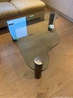Top view of modern glass coffee table showing the clear, thick glass surface and three cylindrical metal legs.