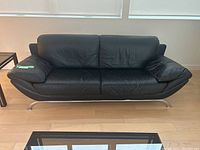 Front view of black leather sofa on light wood floor beneath windows