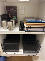 Top shelf with three stainless steel tumblers, Fine Wool sign, manual 3-hole punch, black mesh letter organizer with folders and papers.