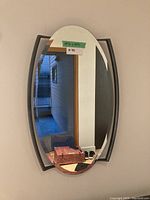 Front view of the oval wall mirror mounted on a wall, with reflections showing nearby doorways and hallway.