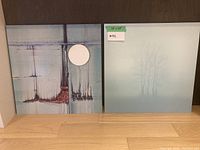 Pair of metal art pieces side-by-side on a wooden floor, showing abstract aqua and gray tree designs