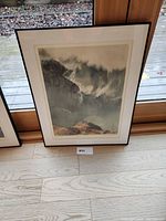 Framed sea inlet print artwork resting against window showing full image, frame and matting, with visible artist signature and numbering below print.