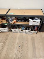 Shelf unit viewed frontally showing particle board shelves and metal frame, with multiple boxes on lower shelf.