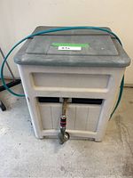 Front view of the Suncast garden hose organizer with green hose wrapped over the lid and metal nozzle attached at the front outlet.