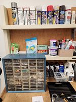 Shelf with multiple aerosol cans including rust preventatives and paint sprays, small hardware drawer cabinet, grout, cleaning products.
