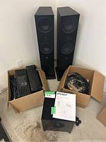 Wide view showing two floor-standing speakers, box of audio components, box of cables and Energy subwoofer