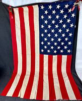 Photo showing full front view of vintage American flag with 50 stars and red and white stripes, hanging vertically