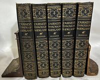 Set of five black leather-bound hardcover books with gold gilt detail and embossed spines, grouped together on a white background with wooden bookends nearby.