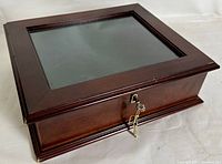 Front view of cherry wood shadow box with visible glass lid and key lock, showing wood grain and polished finish.