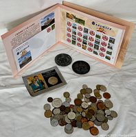 Overview of all items: folded stamp booklet, two large dark coins, and pile of assorted coins.