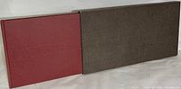 Photo showing the burgundy hardcover art book partially slid out of a dark brown textured slipcase, illustrating the slipcase's protective function and material contrast.