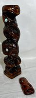 Side view of the taller Maori carved wood tiki totem showing detail of carving and abalone eye inset alongside smaller totem.