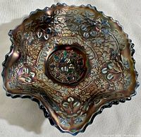Top view showing intricate pressed grapevine and floral pattern with iridescent finish and ruffled blue rim.