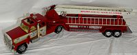 Full side view of the extended red and white steel fire truck toy showing the cab, middle body, and the attached aerial ladder with printed labeling.