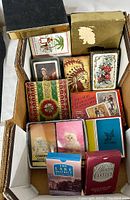 Photo showing various vintage playing card packs in a shoebox, including one with Native American chief illustration, floral design, and others.