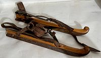 Pair of antique wooden skates with steel blades and leather straps on white background.