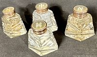 Four vintage cut glass salt and pepper shakers with sterling silver collars and mother of pearl tops arranged on a dark surface, showing top view with holes.