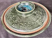 Top view of the covered pottery bowl showing the incised leaf and berry pattern under a thick pooled glaze with a central knob handle.
