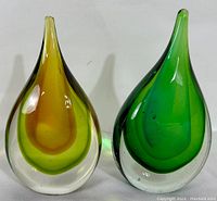 Front view of two Murano Sommerso art glass teardrop sculptures, one in shades of amber and yellow, the other in green, placed side by side.