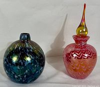 Photo of two vintage art glass pieces, a blue-green iridescent bud vase and a pink perfume bottle with stopper, showing full front view of both items.