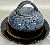 View of the butter dish from the side showing the rounded lid with speckled blue glaze and a black plate base.