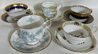 Five vintage English bone china tea cups with matching saucers arranged in cluster showing varied floral and gold decorative patterns.