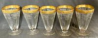 Front view of 5 vintage depression glass parfait glasses showing gold rims and etched decorative pattern on clear glass.