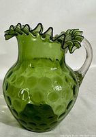 Front side view of vintage green coin dot glass pitcher with clear applied handle and ruffled top edge.