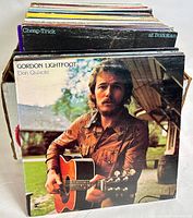 Angle showing multiple vinyl LP records stacked in box, front cover showing Gordon Lightfoot's Don Quixote album with artist holding guitar outdoors.