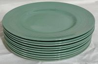 Stack of 10 green ceramic plates with banded rim design, smooth glossy finish.