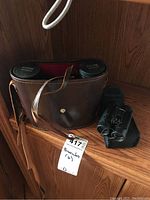 Two pairs of binoculars: a vintage Town and Country binoculars in a worn brown leather case with strap, and a Bushnell compact binoculars with black exterior.
