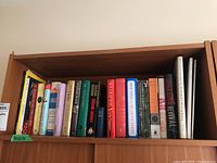 Shelf with 18 assorted books in hardcover and softcover with a range of colors and sizes, titles visible such as 'For the Love of a Dog', 'The Book of Negroes', 'The Edible Woman', 'Surfacing', 'Wives of the East Wind', among others.