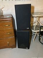 Pair of black Centrex by Pioneer speakers stacked in basement environment next to furniture