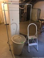Full view of metal clothes rack, plastic laundry hamper, and metal footstool together in a basement.