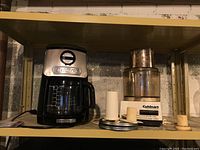 KitchenAid coffee maker and Cuisinart food processor on metal shelf with some attachments placed in front of food processor.