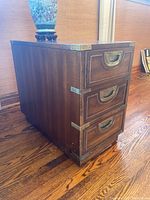 Side view of the wood end table showing the three drawers and brass accents.