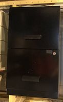 Front view of black coated metal file cabinet with two drawers and handles