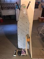 Two ironing boards and clothes steamer arranged in basement. Ironing boards with striped covers and wooden/metal legs visible. Clothes steamer shown with power cord coiled.