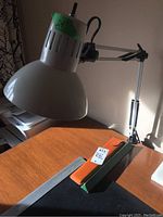 Photo showing the white metal desk lamp with clamp on a wooden desk alongside two measuring tools: a slide rule and ruler in protective sleeves.