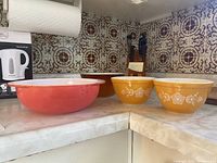 Photo showing the two smaller Pyrex bowls with butterfly gold pattern alongside the large coral-orange Pyrex dish on a kitchen counter.