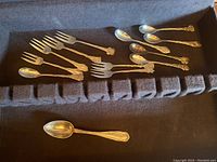 Assorted silver plated forks and spoons with ornate floral design handles laid out in a black fabric-lined storage box.